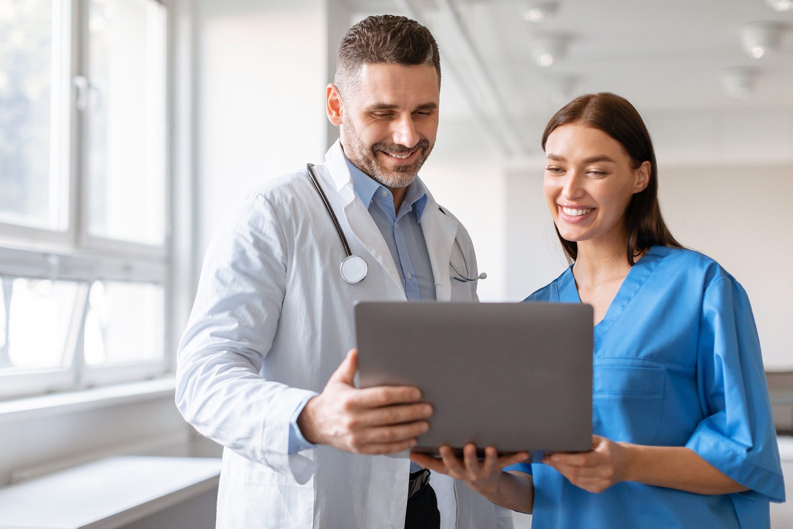 Doctor and nurse smiling and collaborating while looking at a laptop